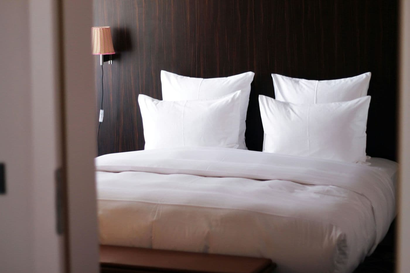 Cama de hotel tendida con sábanas y almohadas blancas